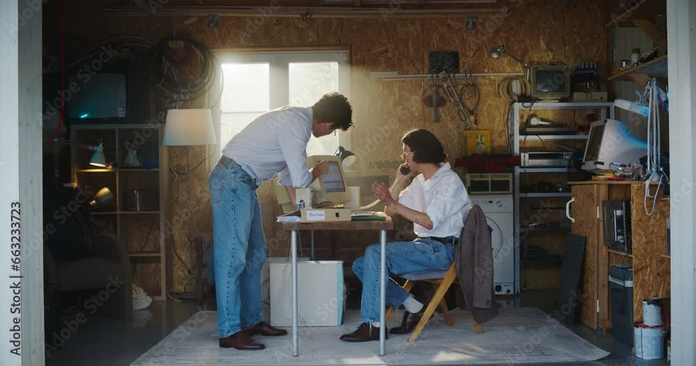 Two Caucasian Male Stock Traders Working In Retro Garage, Using Old Computer With Candlestick Chart And Landline Phone To Pitch A Public Company To Investors. Partners Celebrating Successful Sale. Two Caucasian Male Stock Traders Working In Retro Garage, Using Old Computer With Candlestick Chart And Landline Phone To Pitch A Public Company To Investors. Partners Celebrating Successful Sale.