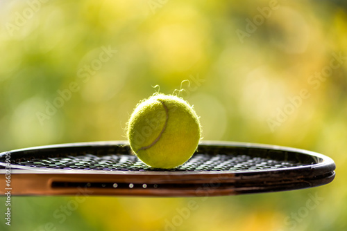 Bright yellow tennis ball and racket with natural light shading on green background at outdoors tennis court, blurred background, copy space. photo
