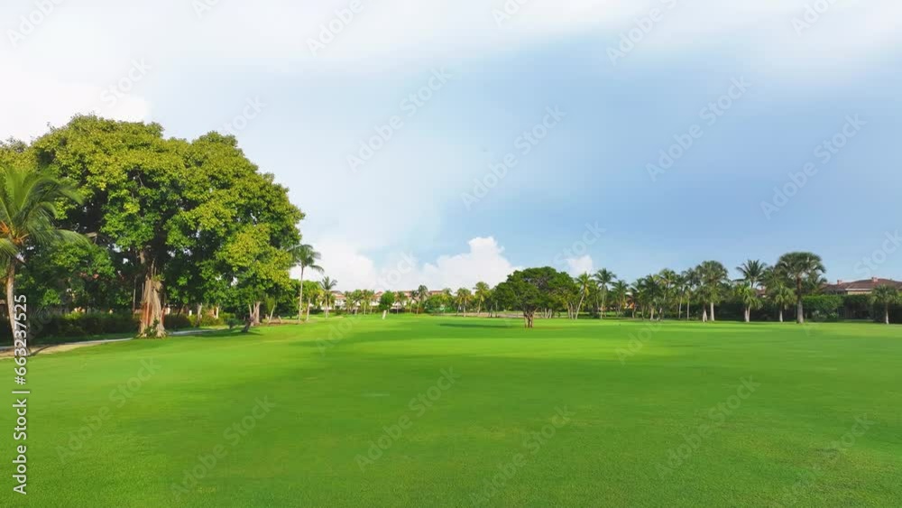 Summer sunny panoramic view of a golf course with green grass lawn and palm trees. Beautiful evening landscape of a golf club with rich green turf. Shadows from palm trees on the grass. Summer sunny panoramic view of a golf course with green grass lawn and palm trees. Beautiful evening landscape of a golf club with rich green turf. Shadows from palm trees on the grass.