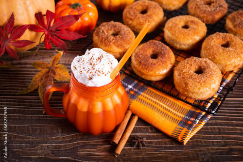 Pumpkin spice whipped latte in glass. Hot autumn drink beverage. Nearby delicious apple cider donuts.