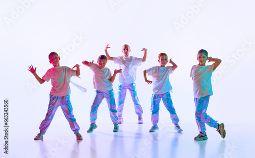 Cute talented children dressed in fashion clothes with bright glittered makeup performing new dance in neon light over white studio background.