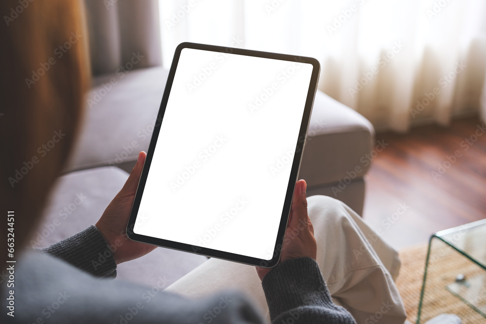 Mockup image of a woman holding digital tablet with blank desktop screen while sitting on a sofa at home Mockup image of a woman holding digital tablet with blank desktop screen while sitting on a sofa at home