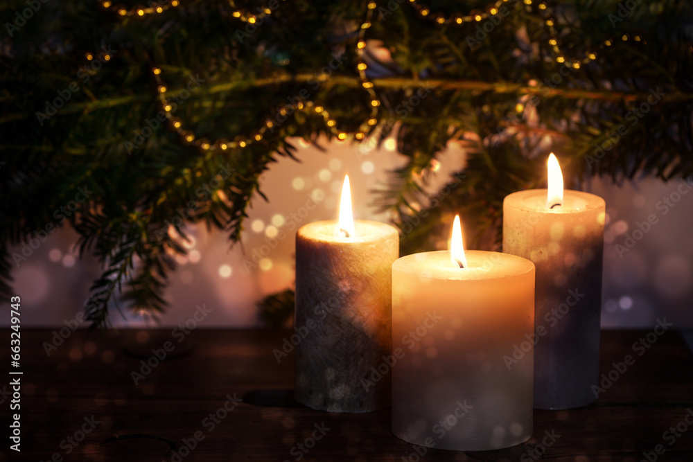 Three burning candles in front of dark fir branches with Christmas decoration and bokeh bubbles, seasonal holiday greeting card, copy space, selected focus