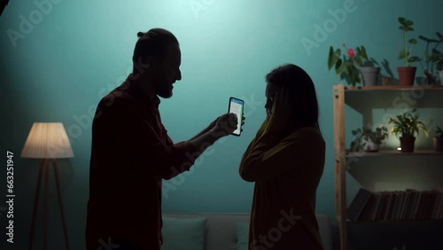 Silhouette of a husband and wife arguing near a wall, a man accusing his girlfriend of adultery, showing a smartphone screen with messages from her lover photo