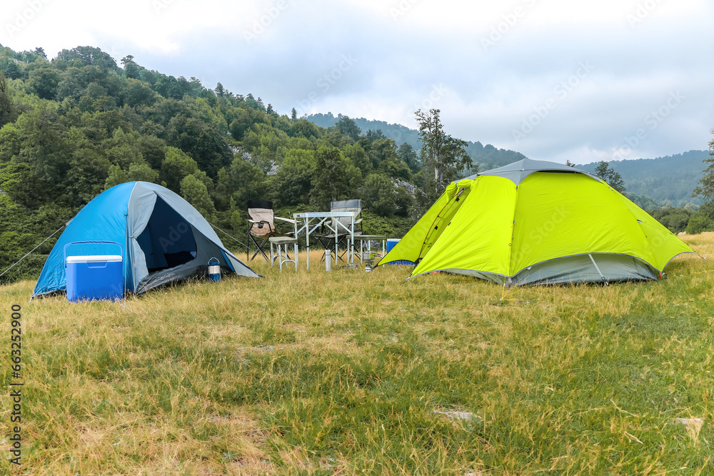 Camping equipment in an empty area with greenery and mountains. Two blue and green tents. A holiday spent in nature with the necessary materials.
