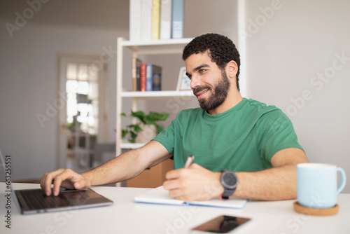 Cheerful young arab man blogger, manager, freelancer at workplace typing on laptop, works remotely