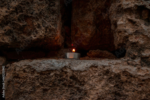 A small candle burning in the dark area among the stones inside the mountain. Background concept. photo