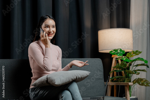 Asian woman in the living room and talking on the phone with friends, female company employee on vacation, spending vacation time and free time relaxing at home, weekend vacation doing activities. #663255970