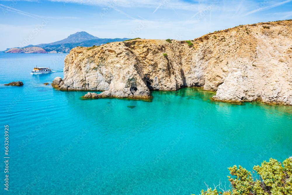 Fototapeta premium View of beautiful rocky coast near Tsigrado beach and boat on azure sea water, Milos island, Cyclades, Greece