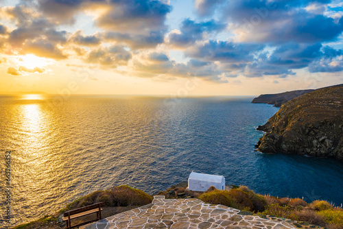 Sunrise over rocky coast of Sifnos island with small church in background in Kastro village, Cyclades, Greece