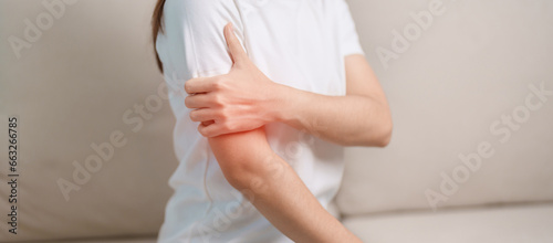 Woman having arm pain during sitting on couch at home, muscle injury and ache. Health and medical concept