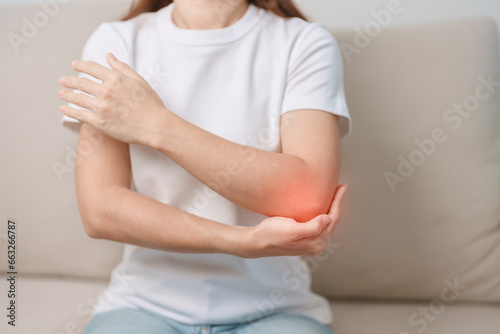 Fotografie Woman having elbow ache during sitting on couch at home, muscle pain due to lateral epicondylitis or tennis elbow