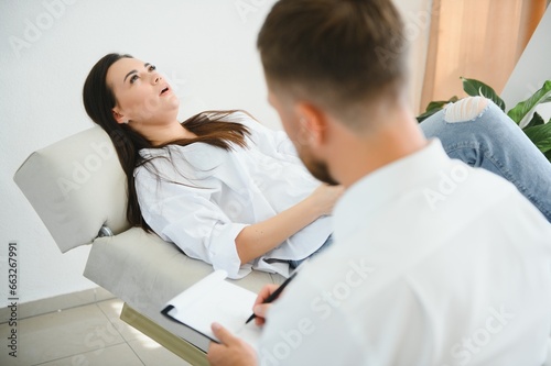 Psychologist taking notes during therapy session with sad young woman in his office. Copy space