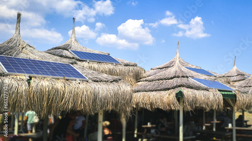 Blue tropical sky and authentic traditional Polynesian thatched roof houses with eco-friendly use of solar panels. View on the beach with a building with a solar panel on the roof. photo