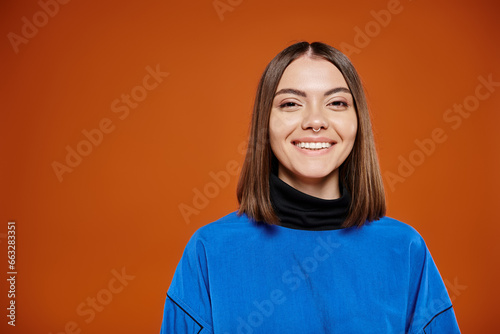 attractive smiley woman in casual blue jacket smiling cheerfully at camera on orange background © LIGHTFIELD STUDIOS
