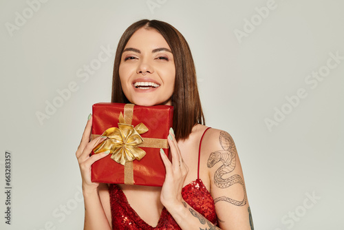 cheerful young woman smiling sincerely and holding red present in hands, holiday gifts concept