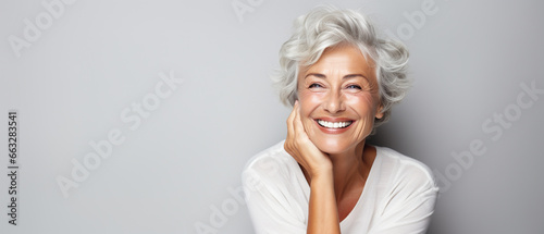Portrait of a happy smiling beautiful aging mature woman with smooth healthy face skin and gray hair on white background with empty copy space