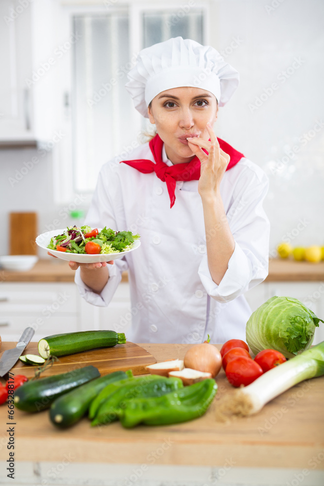 Female chef in white uniform showing approving gesture satisfied with vegetable salad Female chef in white uniform showing approving gesture satisfied with vegetable salad