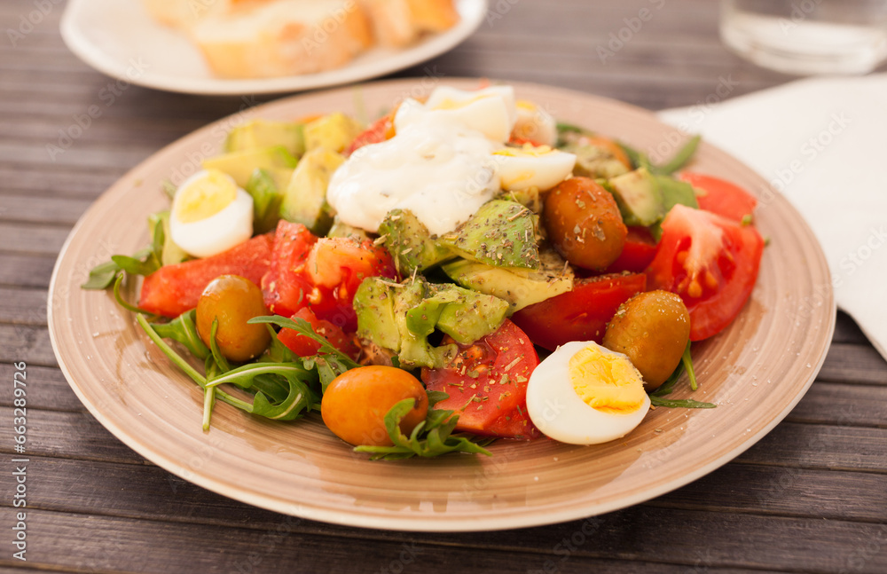 Fresh salad of arugula, avocado, cherry tomatoes with olives and quail eggs on brown plate