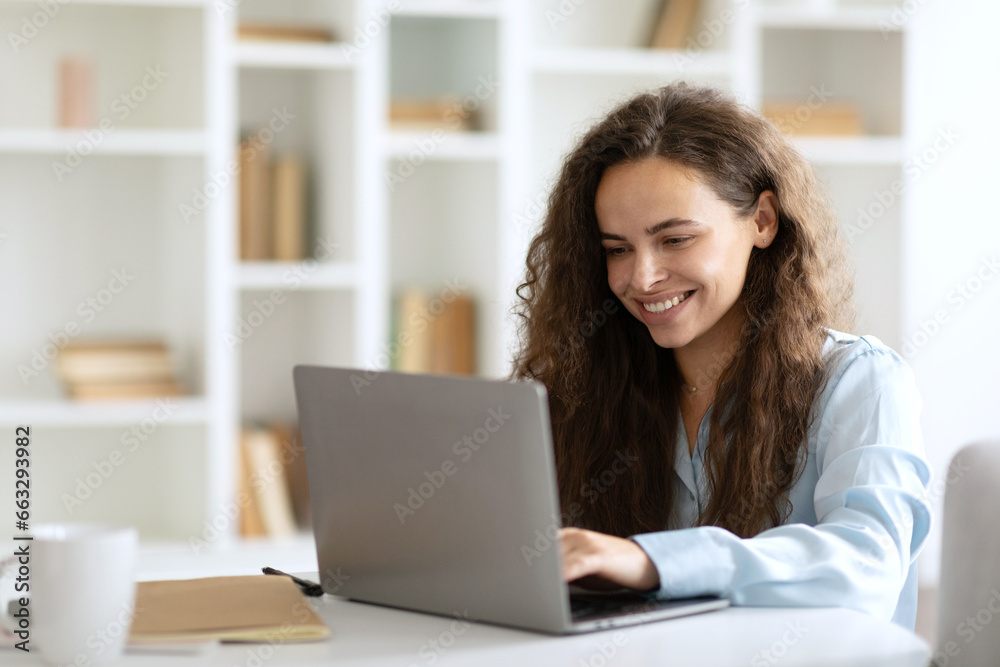 Happy caucasian lady freelancer or entrepreneur working from home, sitting at table in home office, using modern laptop, typing on keyboard, copy space Happy caucasian lady freelancer or entrepreneur working from home, sitting at table in home office, using modern laptop, typing on keyboard, copy space