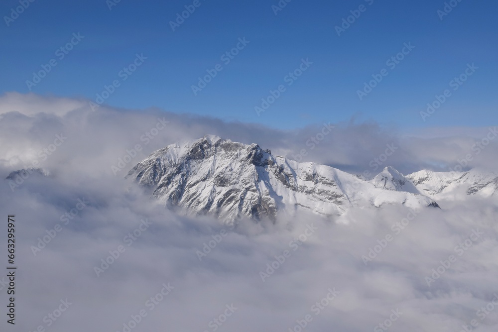Obraz premium Breathtaking aerial view of alpine snowcapped mountain range peaking through heavy clouds. Mountain peaks of the Ötztal Alps from above. The impressive winter view is taken from an airplane window.