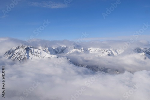 Fototapeta Naklejka Na Ścianę i Meble -  Breathtaking aerial view of alpine snowcapped mountain range peaking through heavy clouds. Mountain peaks of the Ötztal Alps from above. The impressive winter view is taken from an airplane window.