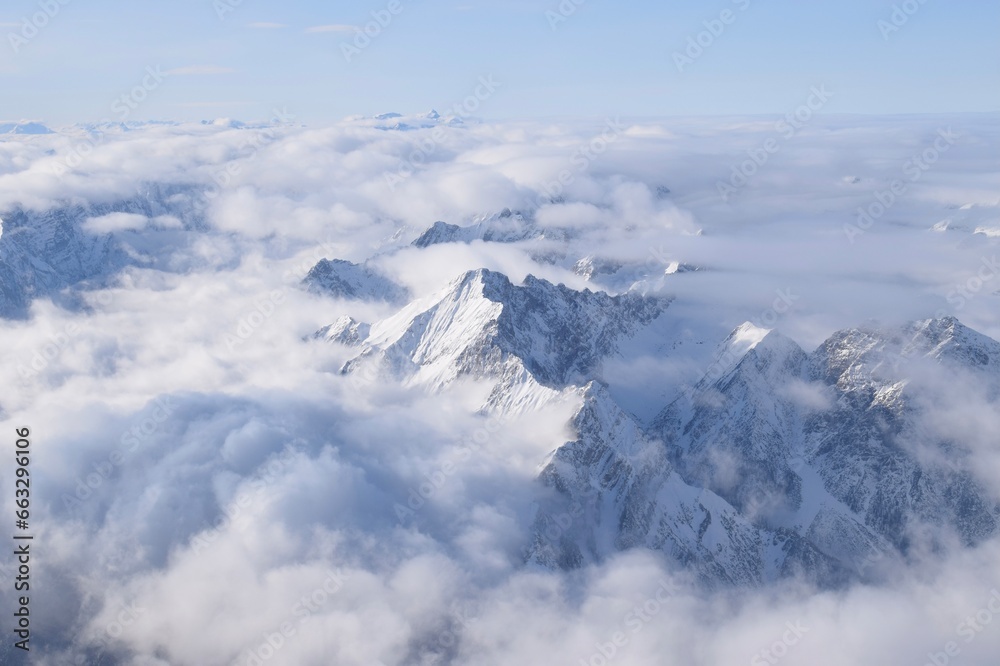 Breathtaking aerial view of alpine snowcapped mountain range peaking through heavy clouds. Mountain peaks of the Ötztal Alps from above. The impressive winter view is taken from an airplane window.