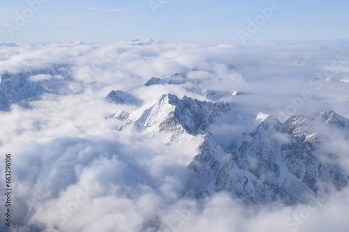 Breathtaking aerial view of alpine snowcapped mountain range peaking through heavy clouds. Mountain peaks of the Ötztal Alps from above. The impressive winter view is taken from an airplane window. © Elenitsa