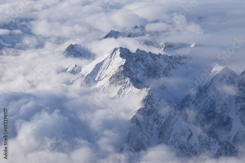 Breathtaking aerial view of alpine snowcapped mountain range peaking through heavy clouds. Mountain peaks of the   tztal Alps from above. The impressive winter view is taken from an airplane window.