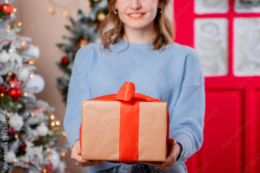 Close-up of a young woman's hands holding a gift, against the background of a Christmas tree. Close-up of a young woman's hands holding a gift, against the background of a Christmas tree.