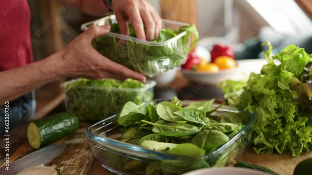 woman adding a spinach leaves to the salad in the kitchen