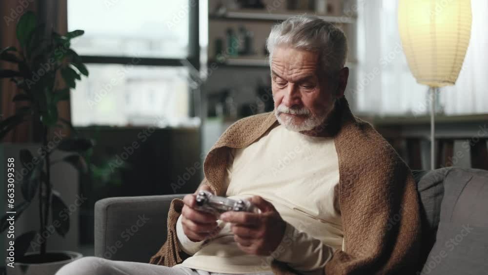 Excited mature gray haired man gamer sitting on a couch and playing in video games on a console at home Happy senior player male controlling joystick for online competition indoors Excited mature gray haired man gamer sitting on a couch and playing in video games on a console at home Happy senior player male controlling joystick for online competition indoors