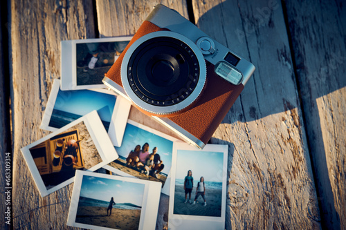 A vintage instant camera and several photographs lie on a wooden table.