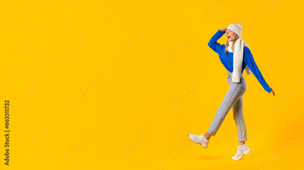 Woman presenting seasonal winter promotional offer, looking at copy space, yellow background, panorama, full length