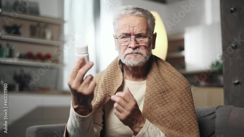 Confused gray haired man reading medical instructions or composition and refuses to take the drug at home Nervous senior male checking pills for ingredients and information and dissatisfied indoors photo