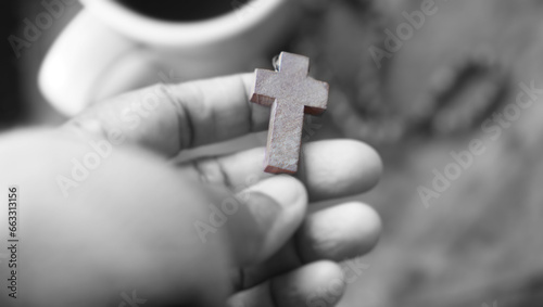 Hand holding wooden cross of Jesus Christ in black and white. Praying rosary concept. Christianity catholic symbol of faith.