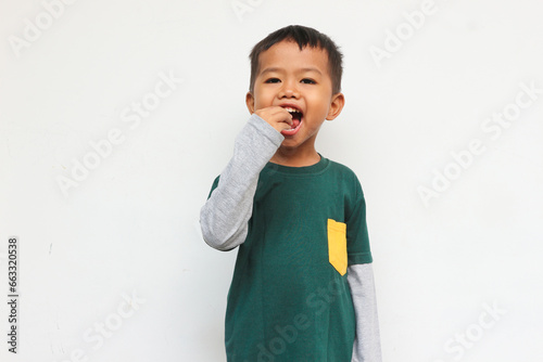 Cheerful boy wearing green layered long sleeve t-shirt standing while showing eat gesture