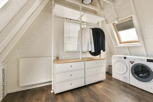 a small laundry room with white cabinets and washer in the corner on the wall is a window that looks out to the sky