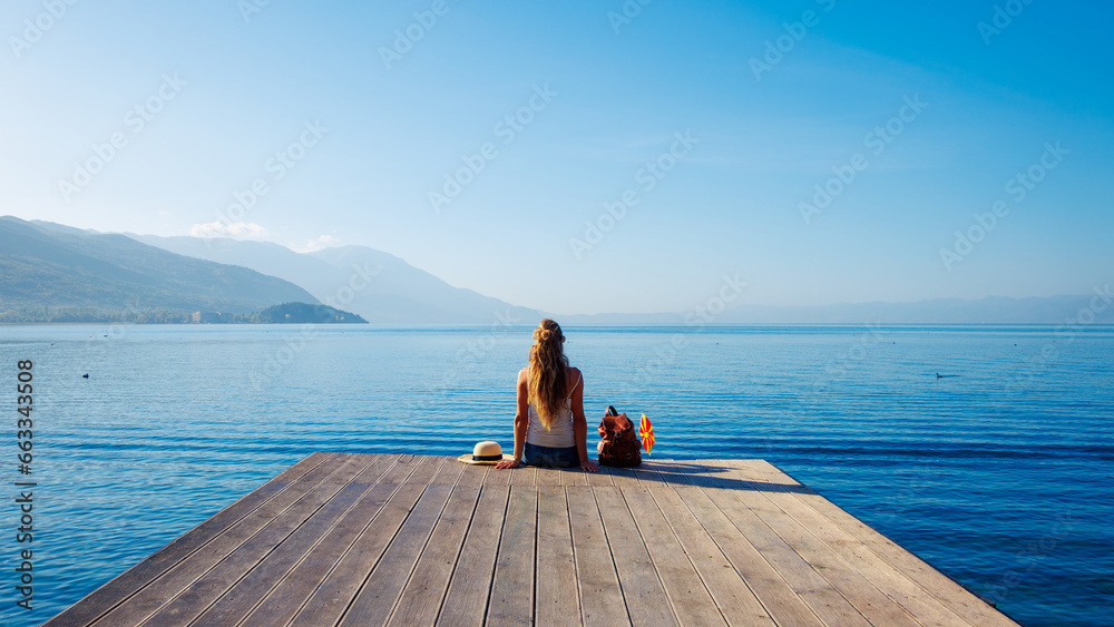 Woman sitting on wooden pier at Ohrid lake shore in Macedonia- tour tourism,travel destination,vacation concept - obrazy, fototapety, plakaty 