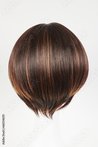 Natural looking dark brunet wig on white mannequin head. Short brown hair on the plastic wig holder isolated on white background, back view.