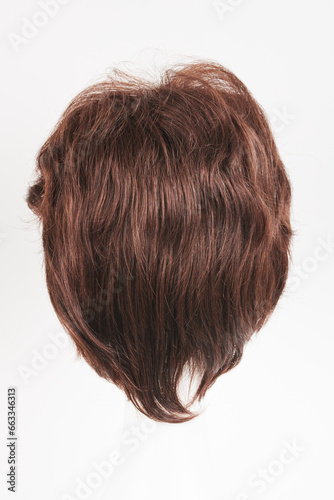Natural looking dark brunet wig on white mannequin head. Short brown hair on the plastic wig holder isolated on white background, back view.