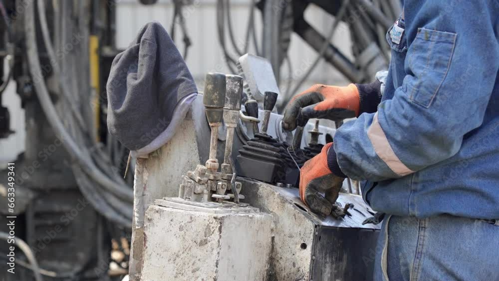 An unrecognizable builder is operating control levers on a drilling machine for efficient construction operations, close-up hands. An unrecognizable builder is operating control levers on a drilling machine for efficient construction operations, close-up hands.