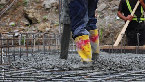 Worker pours concrete from a pipe onto the foundation of a building under construction, close-up of worker's feet.
