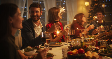 Parents, Children and Friends Enjoying Christmas Dinner Together in a Cozy Home in the Evening. Relatives Sharing Meals, Singing Traditional Festive Songs and Burning Sparkles