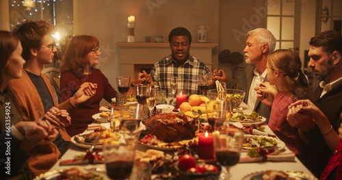 Portrait of a Young Black Man Sitting at a Festive Table with Family and Friends  Praying Before Eating a Turkey Dinner. Religious African Male Blessing Christmas Food  Thanking God and Jesus Christ