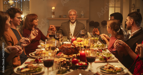 Religious Family Celebrating Christmas at Home. Relatives and Friends Praying and Holding Hands, Blessing Food Before Eating Dinner. Christians Thanking God for Providing a Delicious Turkey Roast © Gorodenkoff