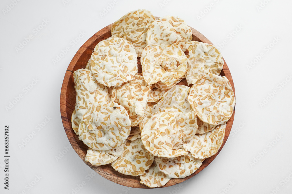 Keripik Tempe or Tempeh Chips are made from soybeans and served on a wooden plate. Isolated on white background. Keripik Tempe or Tempeh Chips are made from soybeans and served on a wooden plate. Isolated on white background.