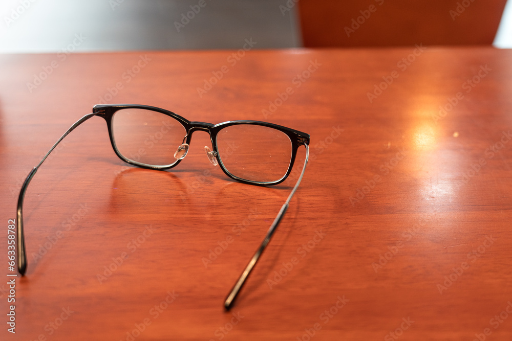 A classic design eyeglasses is placed on the wooden table. Resting from stress business working concept scene. Close-up at object and selective focus. A classic design eyeglasses is placed on the wooden table. Resting from stress business working concept scene. Close-up at object and selective focus.