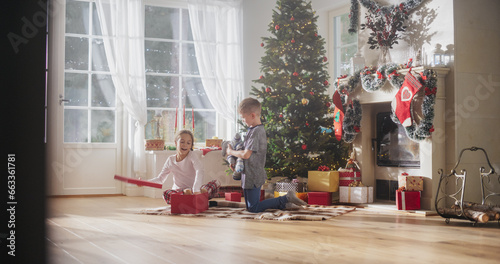 Cute Children Impatient to Get Their Gifts from Under the Christmas Tree at Home. Happy Little Boy and Girl Waking Up on Holiday Morning to Receive New Toys © Gorodenkoff