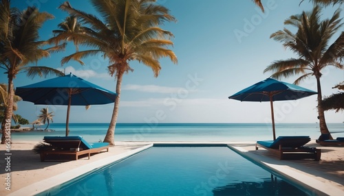 Beach and sea view with luxurious swimming pool, loungers umbrellas, palm trees and blue sky